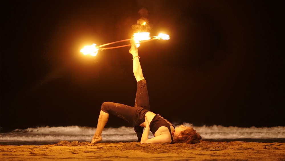 Feuerkünstlerin balanciert nachts am Strand einen brennenden Feuer-Hula-Hoop auf dem Fuß